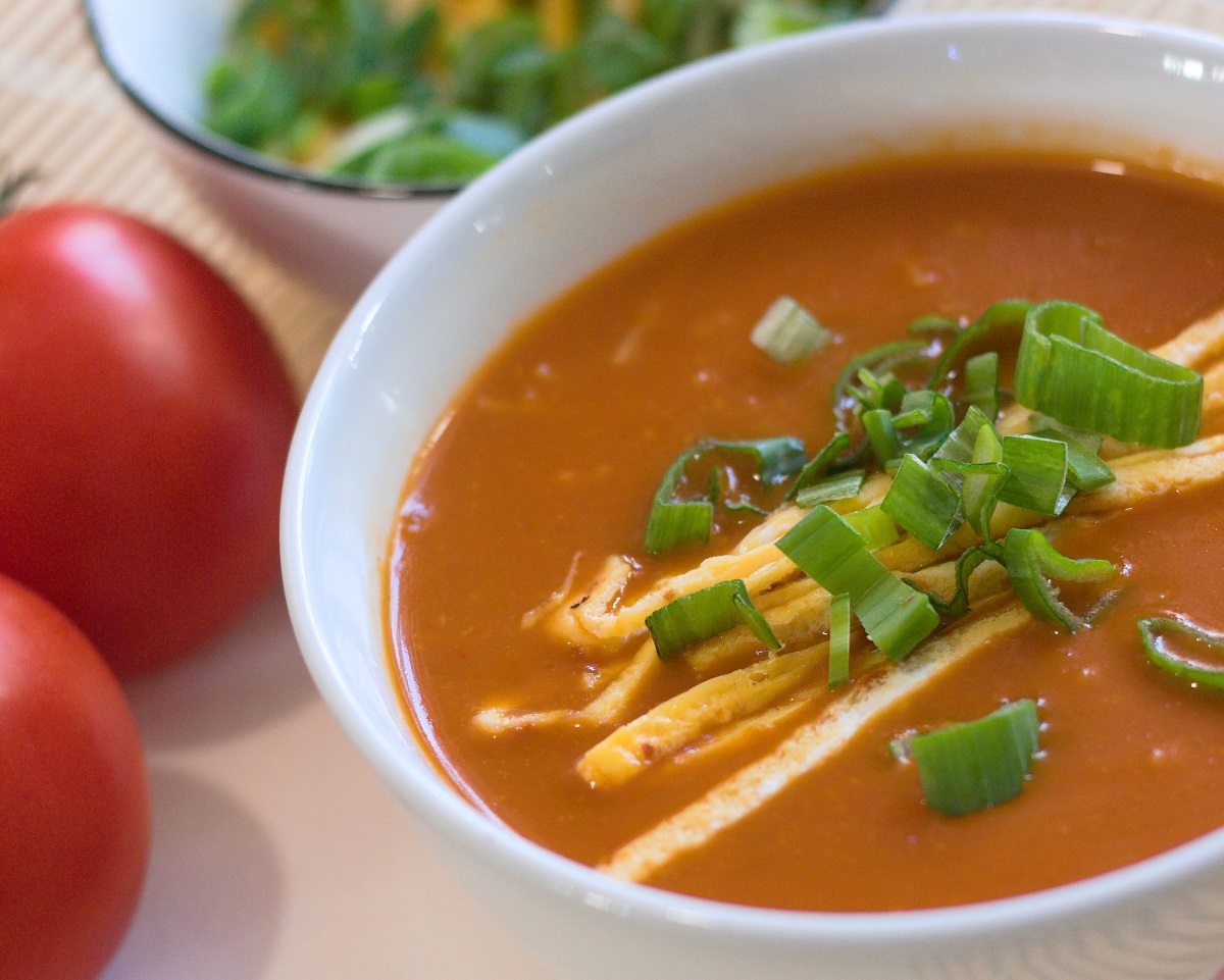 Bowl of spicy tomato soup with omelette strips and spring onion.